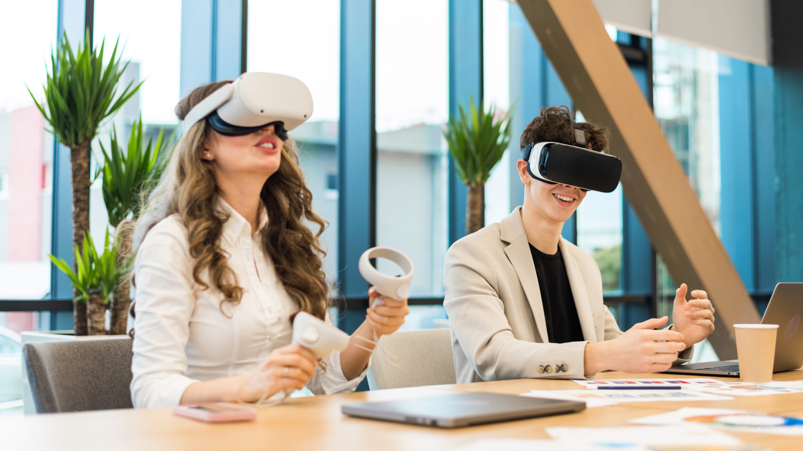 Business conference in VR in an office. A young man and woman using VR glasses and controllers, papers and gadgets on the table